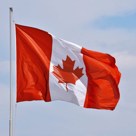 National flag of Canada flying and waving in the wind on flagstaff over clear blue sky, symbol of Canadian patriotism, low angle, side view